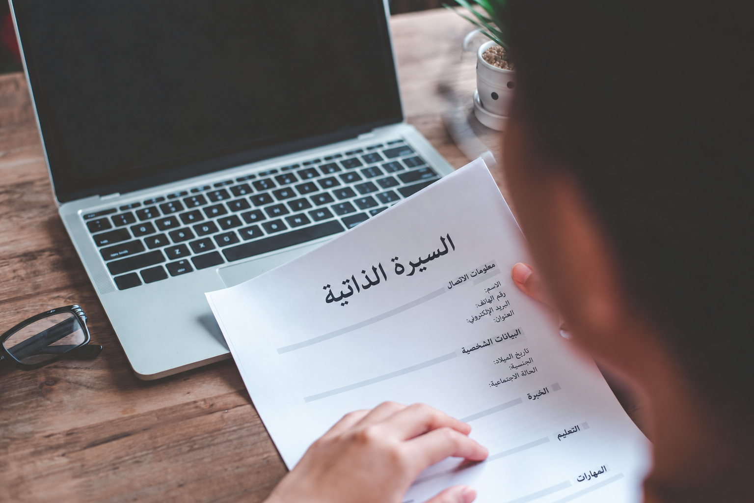 شخص يراجع سيرة ذاتية مطبوعة بجوار حاسوب محمول شخص يراجع سيرة ذاتية مطبوعة بجوار حاسوب محمول
