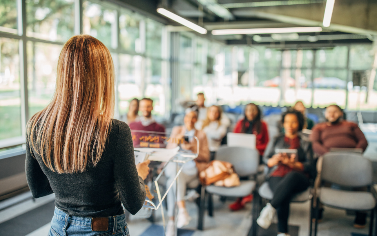Jeune femme de dos en train de présenter devant une classe