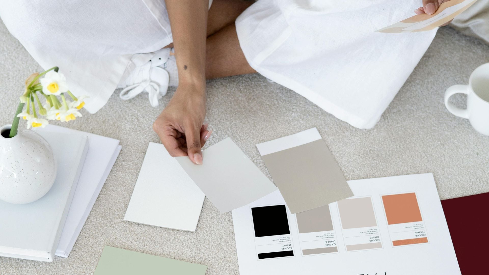 Personne habillée en blanc assise par terre en train de choisir des couleurs pour créer une charte graphique