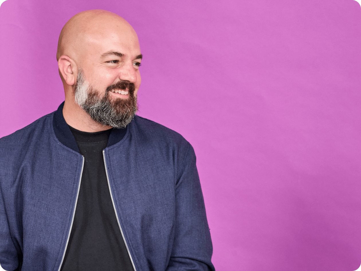 Andrew Green, Head of Design at Canva in front of a magenta background, smiling