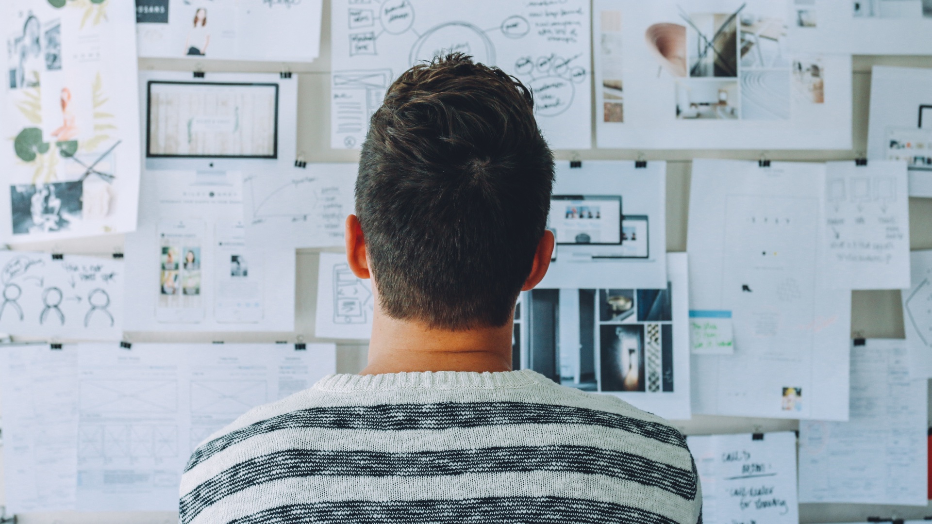 Personne vue de dos en train de regarder un tableau blanc recouvert de notes, de schémas et de documents professionnels